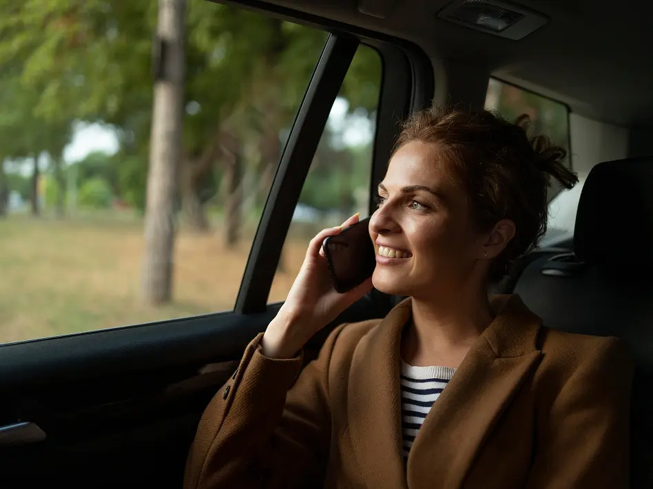 Smiling woman enjoying a comfortable cab ride while talking on phone – airport transfer and outstation taxi service.