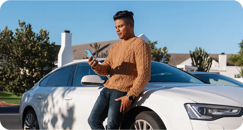 Confident man standing beside a white car using a smartphone